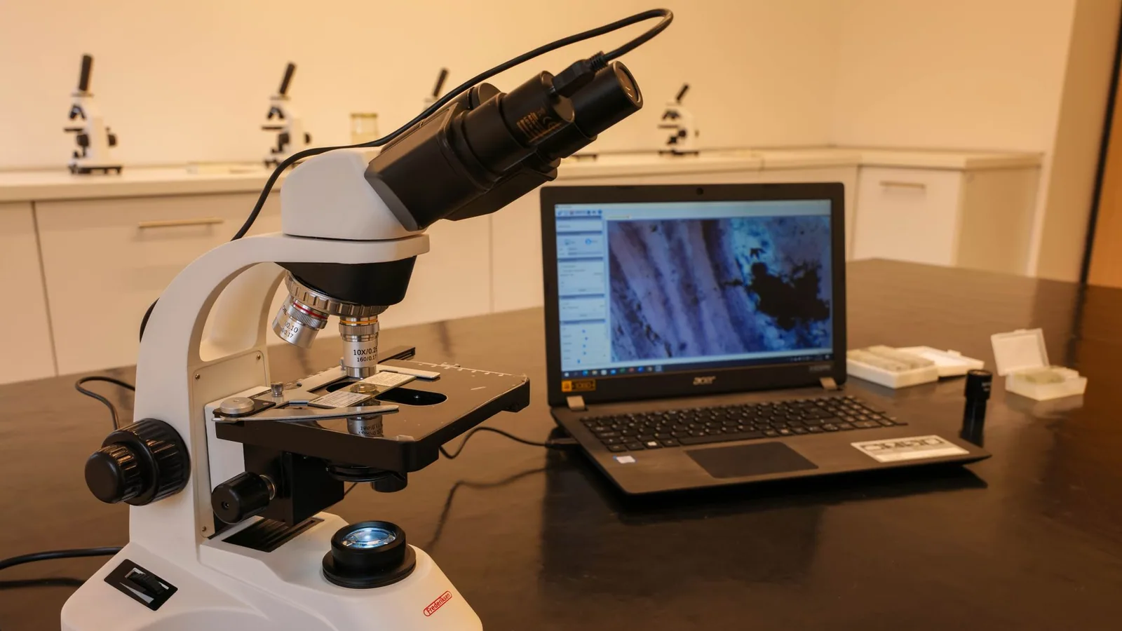 Close-up of a microscope connected to a laptop in a laboratory environment