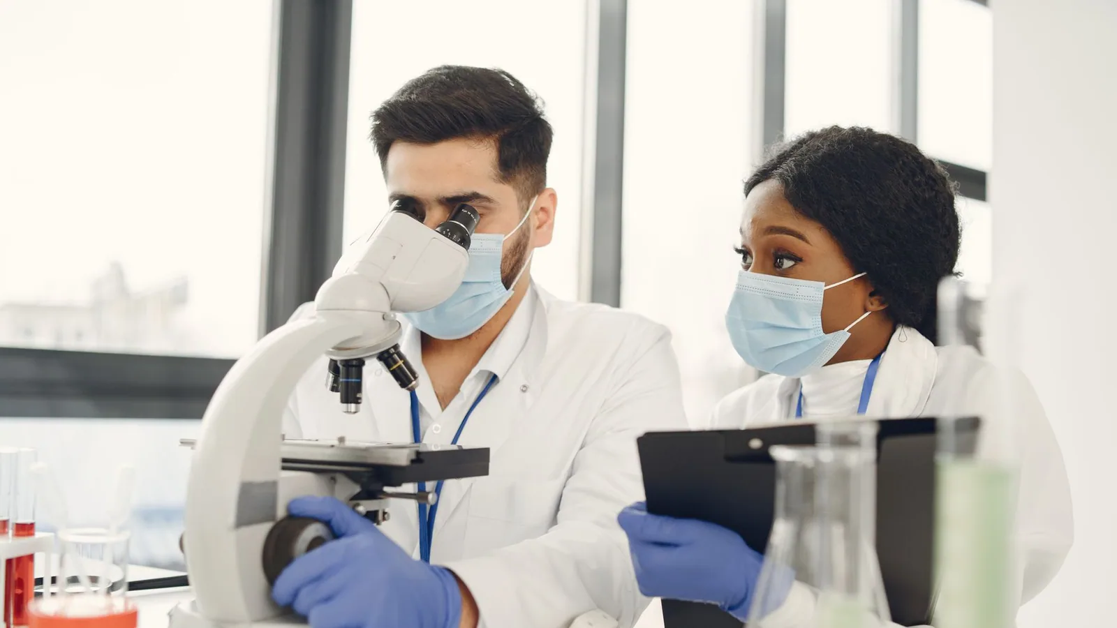 Researchers using a microscope and taking notes in a modern lab