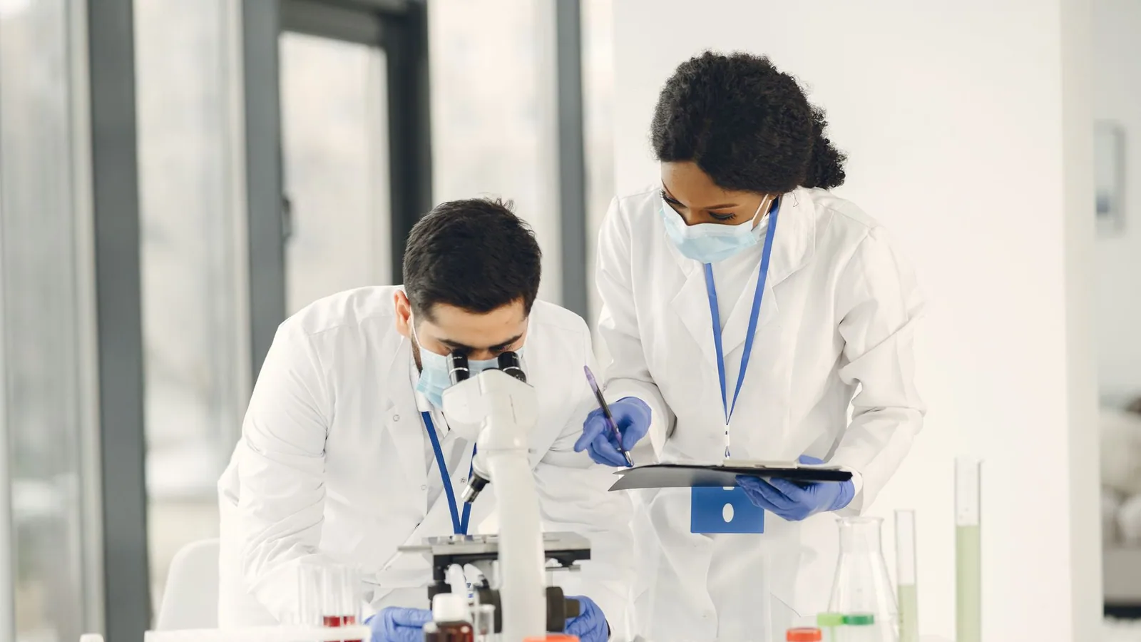Researchers in lab coats and masks working with microscope and test tubes in a laboratory setting
