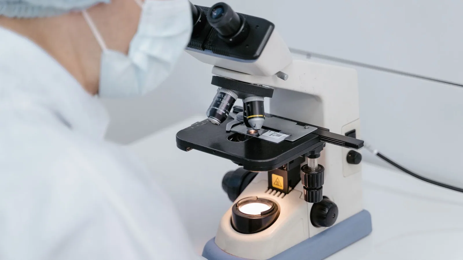 Scientist using a microscope in a laboratory setting, wearing protective gear
