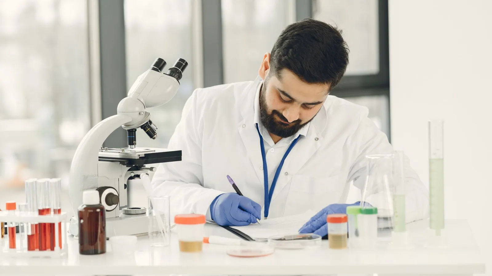 Scientist focused on writing notes amidst laboratory glassware and a microscope