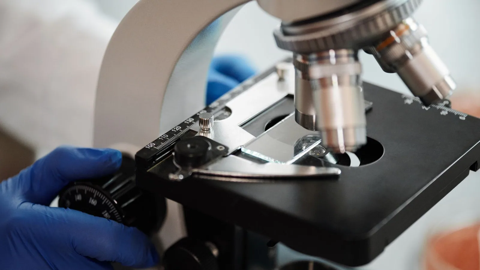 Close-up image of a scientist's gloved hand adjusting a microscope in a research lab