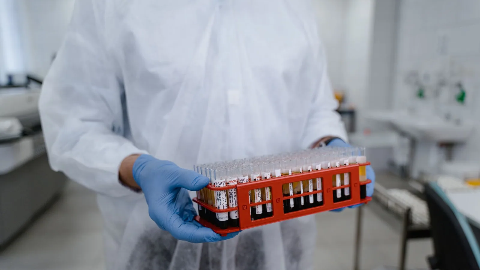 Scientist in protective gear holding a rack of test tubes in a laboratory setting, highlighting research work